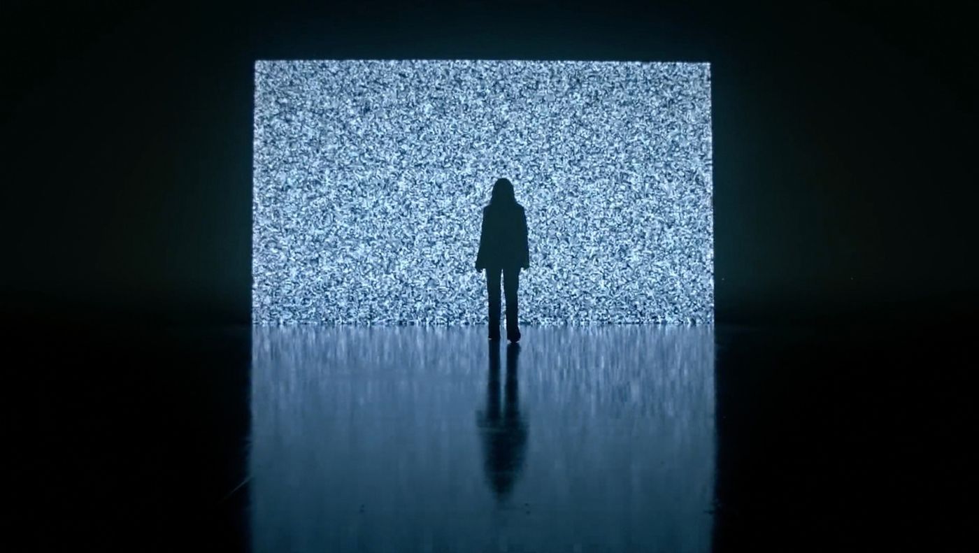 A figure standing before a wall of static light